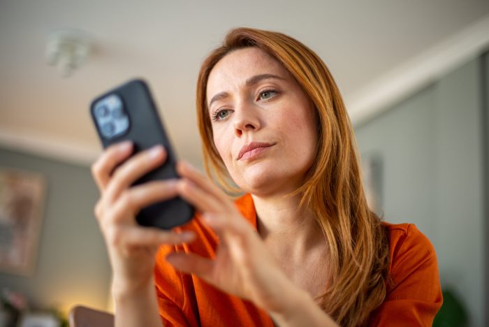 Low angle view portrait of serious woman looking at the mobile phone, sitting at home.